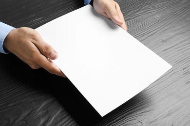 Man holding blank paper sheets for brochure at black wooden table. Mock up