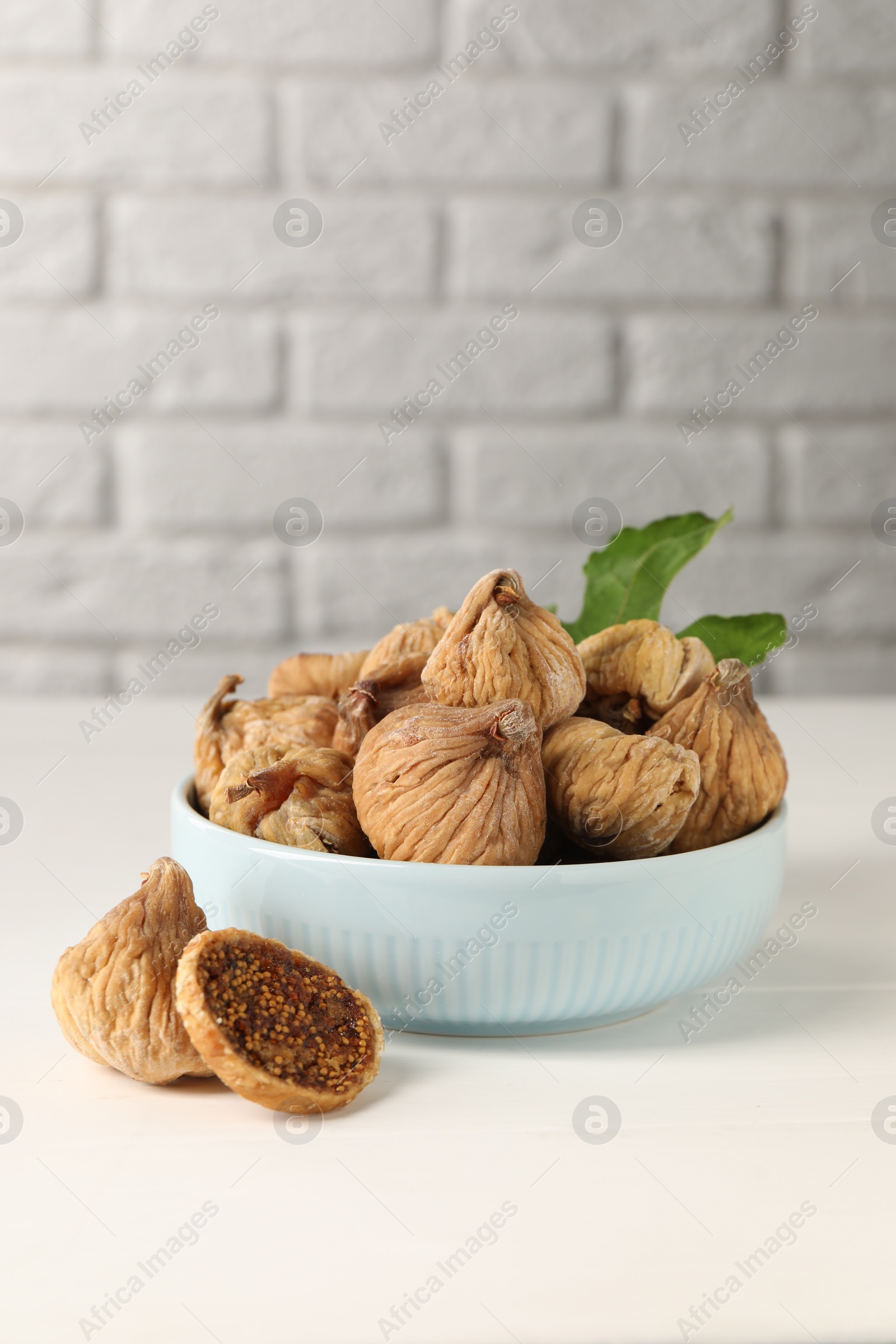 Photo of Bowl with tasty dried figs and green leaf on white wooden table