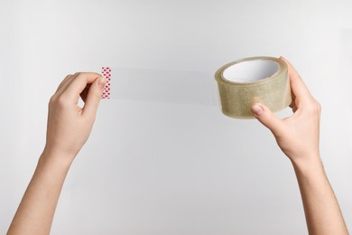 Photo of Woman holding transparent adhesive tape on light grey background, closeup