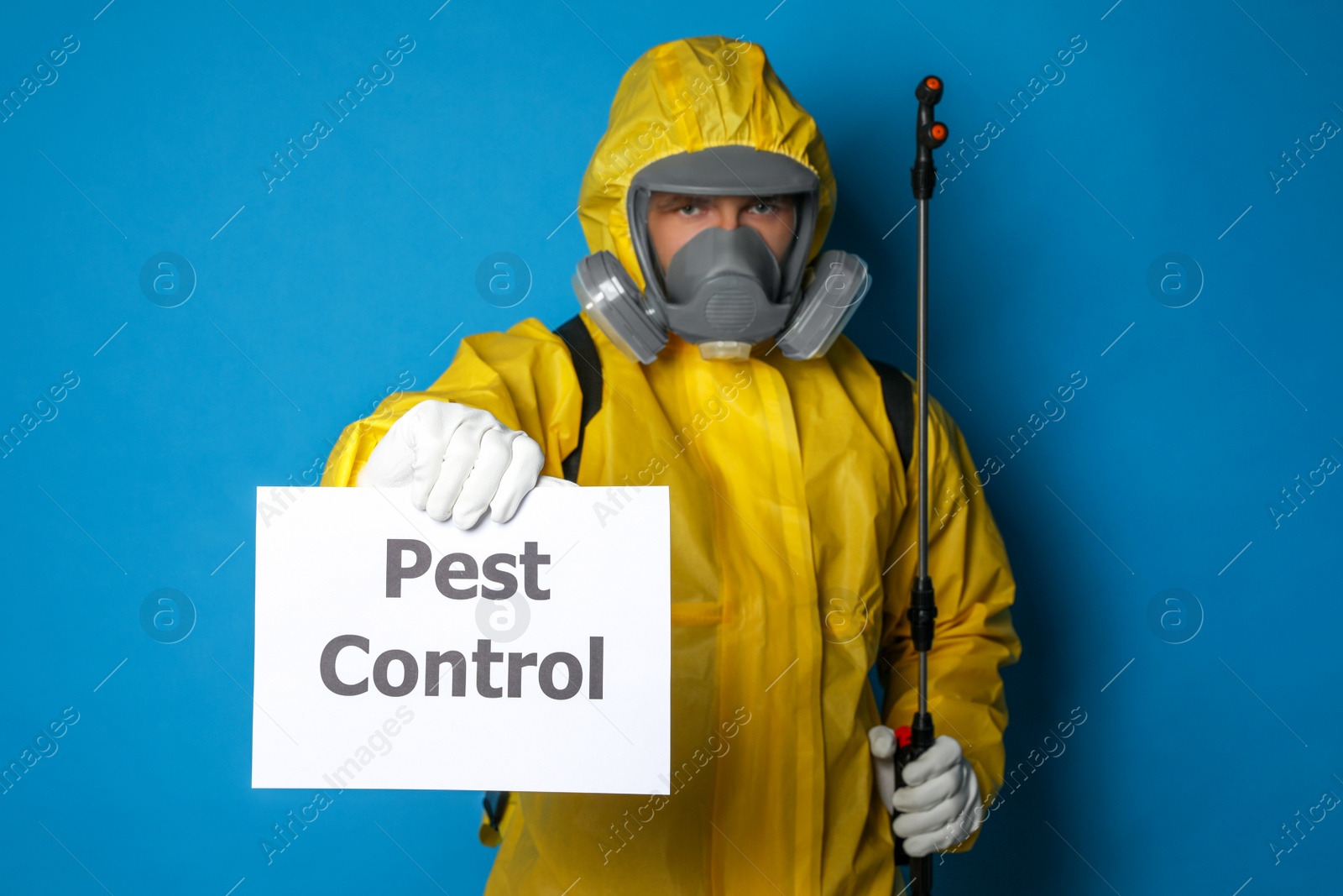 Photo of Man wearing protective suit with insecticide sprayer holding sign PEST CONTROL on blue background