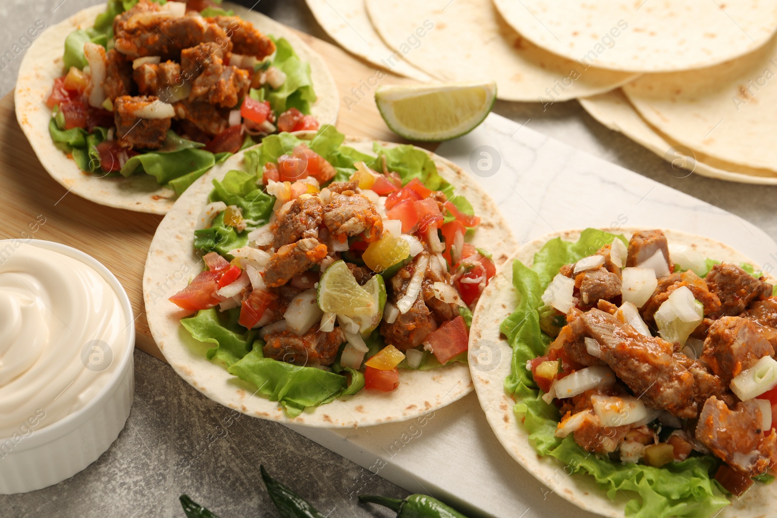 Photo of Delicious tacos with vegetables, meat and lime on grey textured table