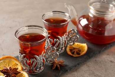 Photo of Slate plate with glasses of traditional Turkish tea in vintage holders, dried orange and anise on light grey table, closeup