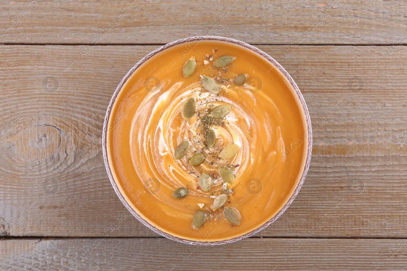 Photo of Bowl of delicious pumpkin soup with seeds and cream on wooden table, top view