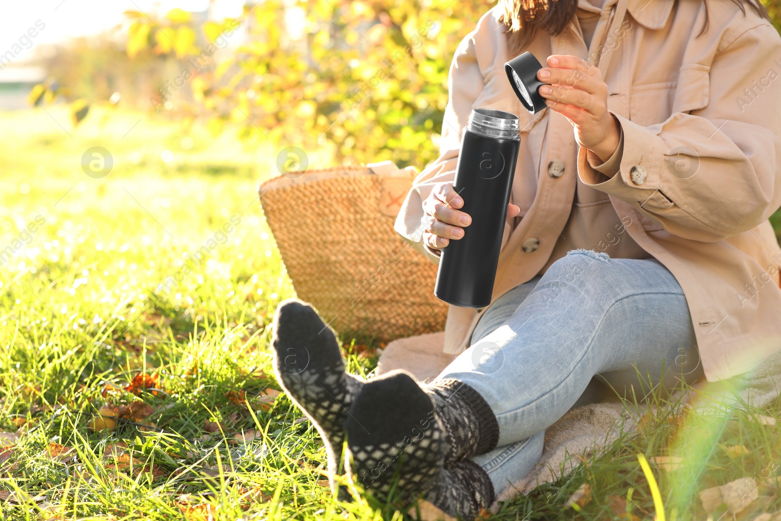 Photo of Picnic time. Woman opening thermos on green grass outdoors, closeup. Space for text