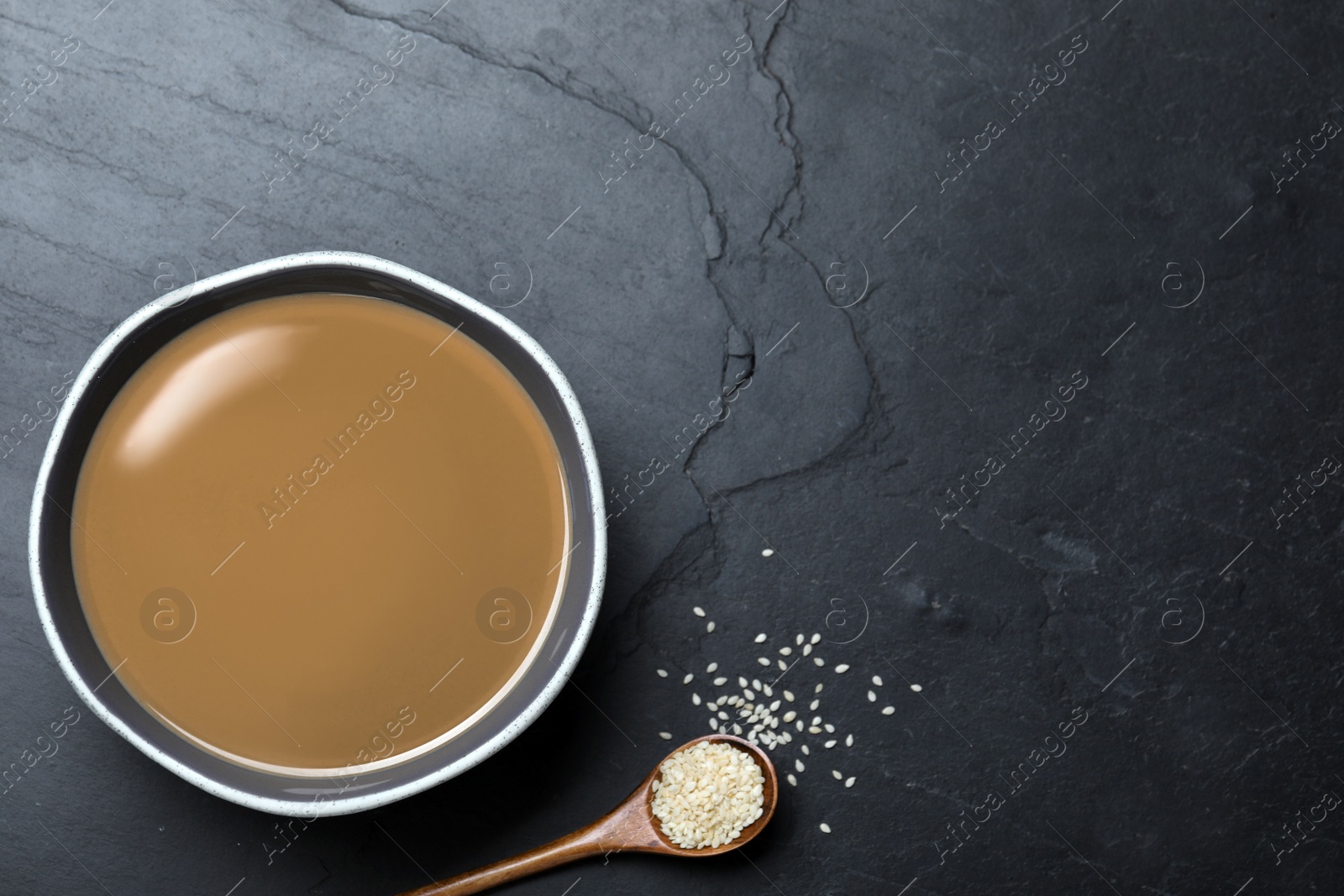 Photo of Tasty sesame paste, spoon and seeds on black table, flat lay. Space for text