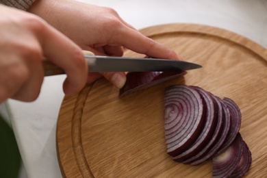 Photo of Woman cutting red onion into slices at countertop in kitchen, closeup