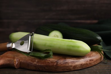 Fresh cucumbers and peeler on wooden table, closeup