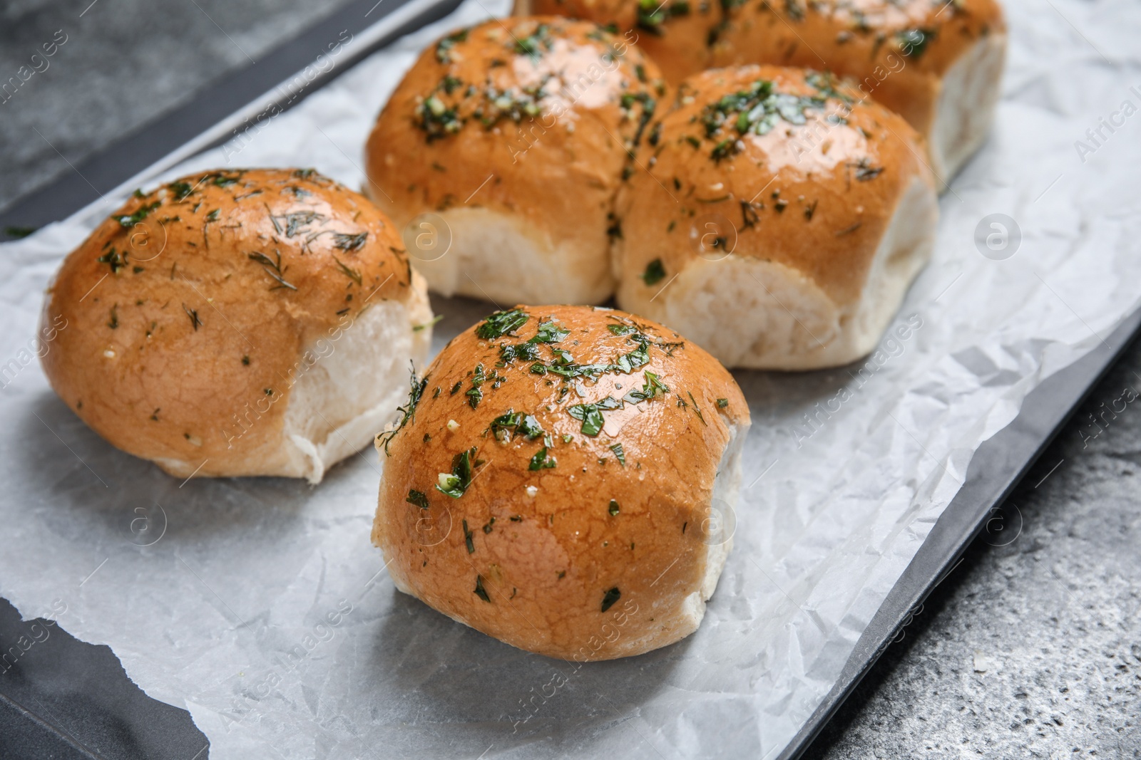 Photo of Traditional pampushka buns with garlic and herbs on baking dish, closeup