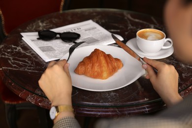 Photo of Woman with tasty croissant at black table, closeup