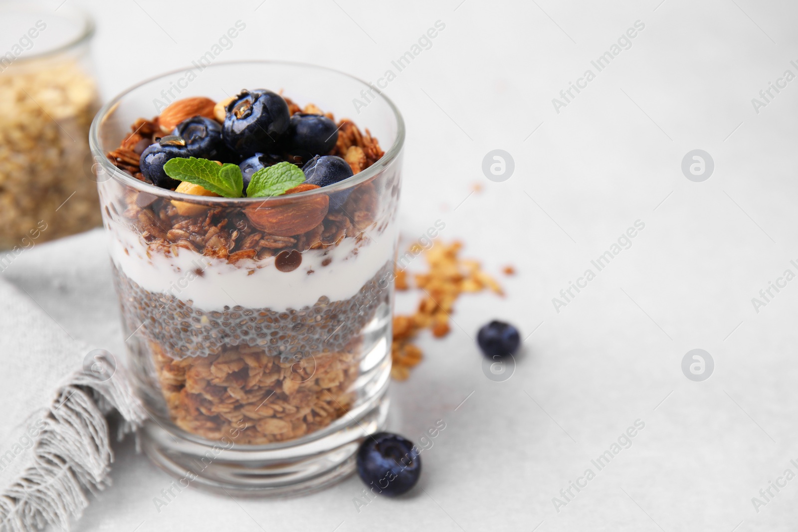 Photo of Tasty granola with berries, nuts, yogurt and chia seeds in glass on light table, space for text