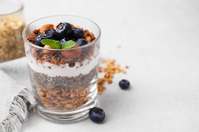 Photo of Tasty granola with berries, nuts, yogurt and chia seeds in glass on light table, space for text