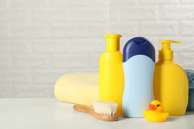 Photo of Baby cosmetic products, bath duck, brush and towel on white table against brick wall. Space for text