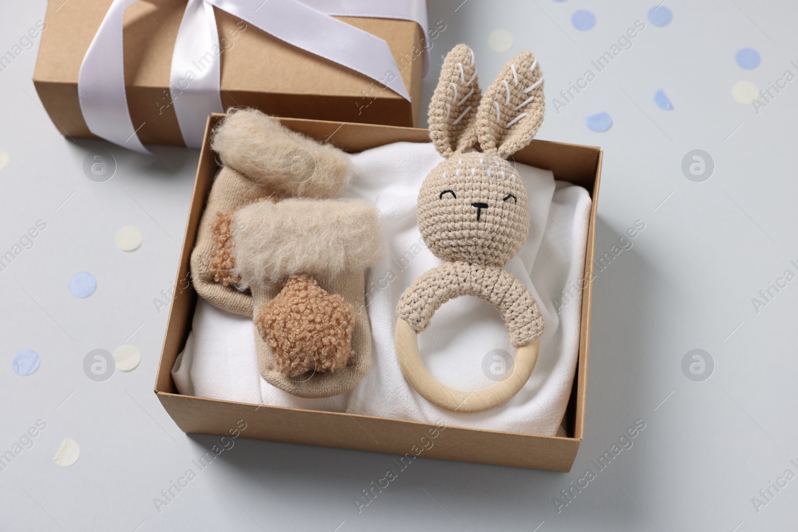 Photo of Different baby accessories in box and confetti on light grey background, above view