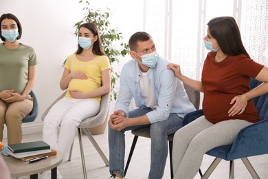 Photo of Pregnant women and man with protective masks at courses for expectant parents indoors