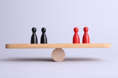 Photo of Equality concept. Seesaw scale with game pieces on light background