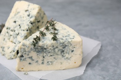 Photo of Tasty blue cheese with thyme on grey table, closeup. Space for text