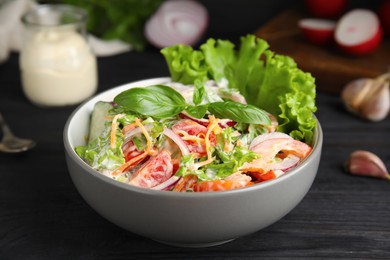 Photo of Bowl of delicious vegetable salad dressed with mayonnaise on black wooden table, closeup