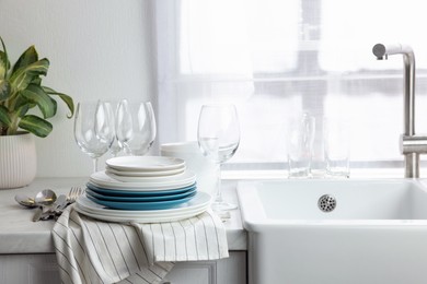 Photo of Different clean dishware, cutlery and glasses on countertop near sink in kitchen, space for text
