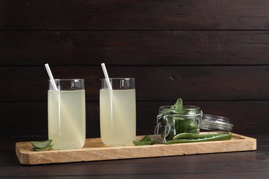 Photo of Tasty aloe juice in glasses and cut fresh leaves on wooden table