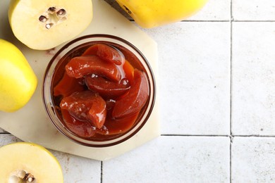 Tasty homemade quince jam in bowl and fruits on tiled table, flat lay. Space for text