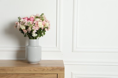 Photo of Beautiful bouquet of fresh flowers in vase on wooden table near white wall, space for text