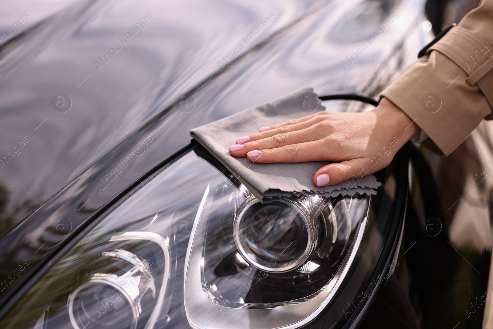 Photo of Woman wiping her modern car with rag, closeup