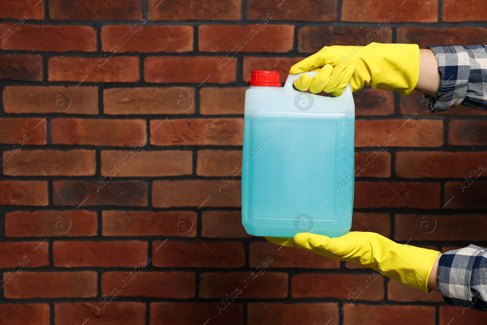 Photo of Man in rubber gloves holding canister with blue liquid near brick wall, closeup. Space for text