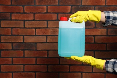 Man in rubber gloves holding canister with blue liquid near brick wall, closeup. Space for text