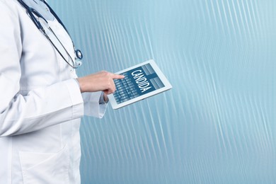 Image of Doctor holding modern tablet with word Candida on light blue background, closeup