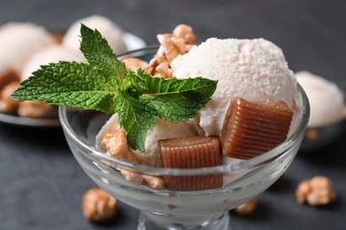 Photo of Glass bowl of ice cream with caramel candies, popcorn and mint on grey table, closeup