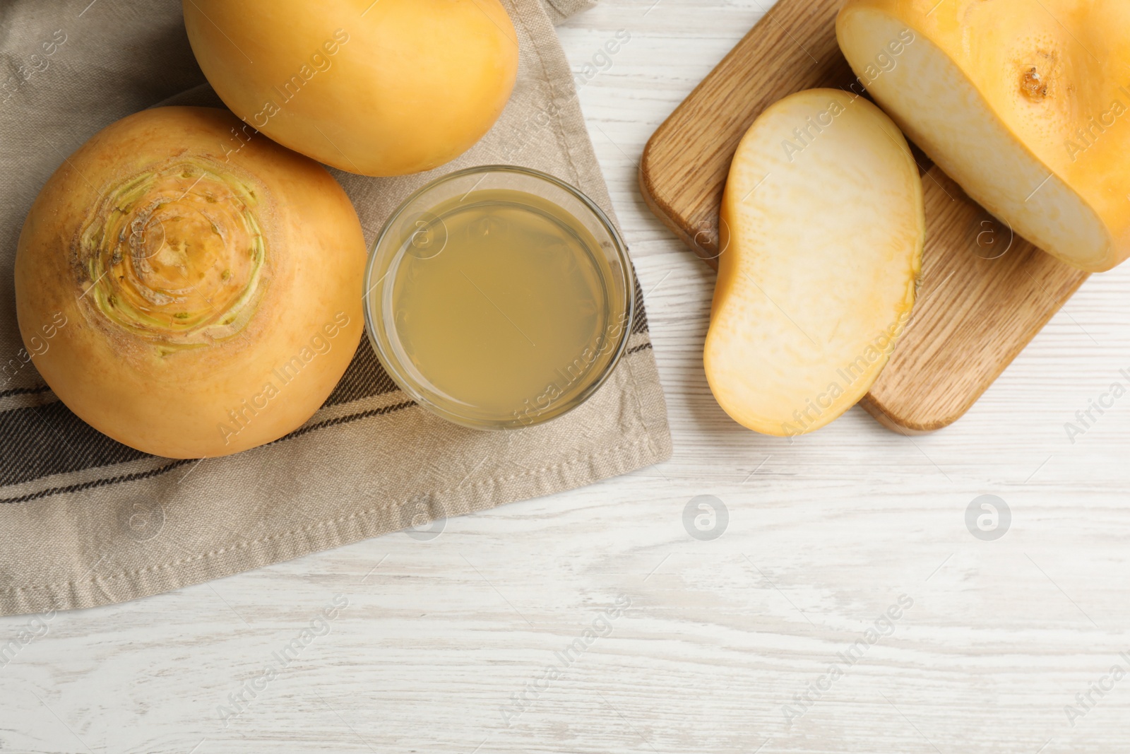 Photo of Glass of fresh natural turnip juice, cut and whole roots on white wooden table, flat lay. Space for text