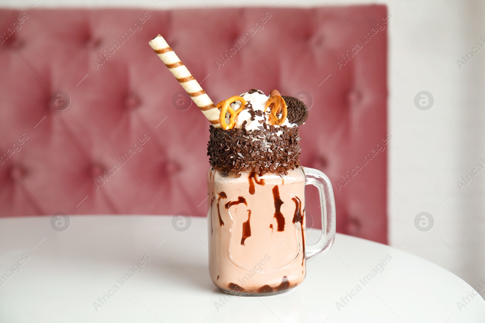 Photo of Tasty milk shake with sweets in mason jar on table at cafe