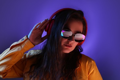 Photo of Portrait of beautiful young woman with headphones on color background with neon lights