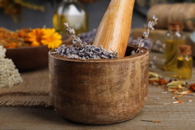Photo of Mortar with pestle and dry lavender flowers on wooden table, closeup. Medicinal herbs