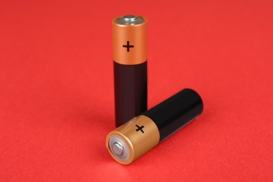 Image of Two new AA batteries on red background, closeup