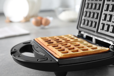 Modern iron with tasty Belgian waffles on grey table, closeup