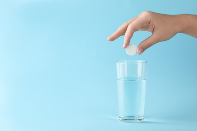 Photo of Woman putting tablet into glass of water on light blue background, space for text