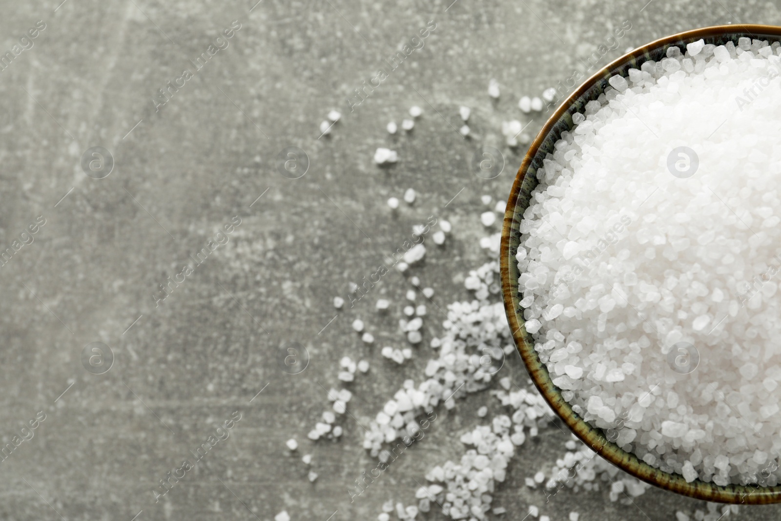 Photo of Bowl of natural sea salt on grey table, top view. Space for text