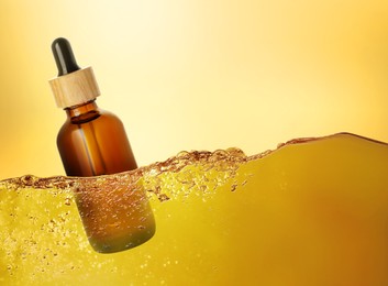 Image of Bottle of cosmetic product floating in essential oil against gold gradient background