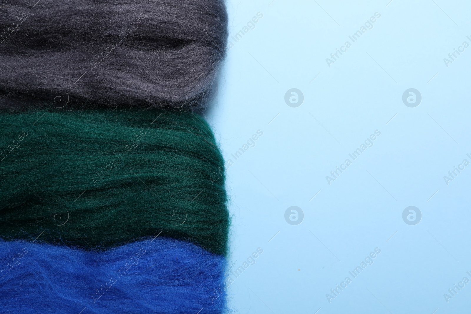 Photo of Colorful felting wool on light blue background, flat lay. Space for text
