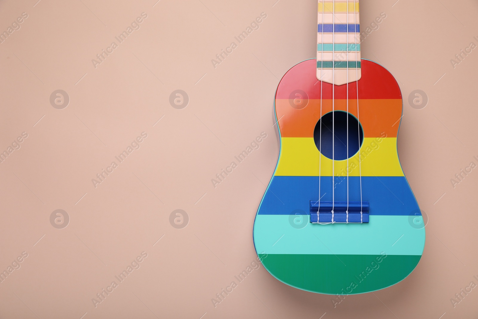 Photo of Colorful ukulele on beige background, top view and space for text. String musical instrument