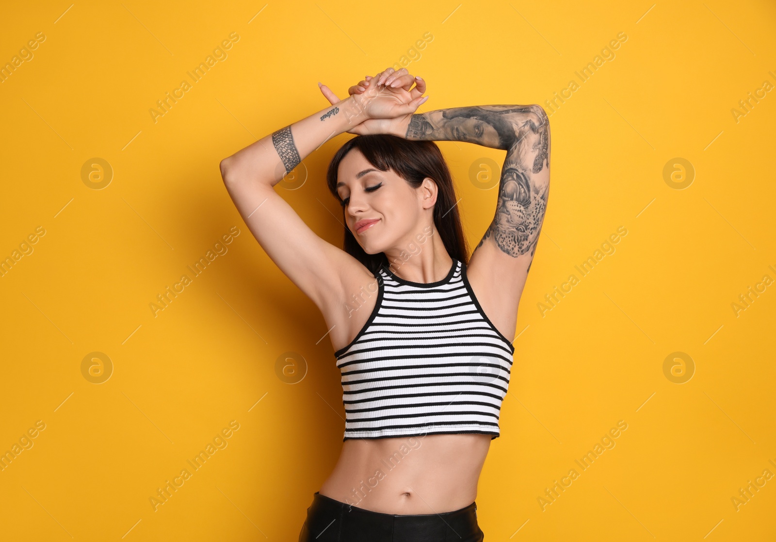 Photo of Beautiful woman with tattoos on arms against yellow background