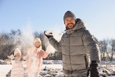 Portrait of smiling man and his family playing snowballs in winter park