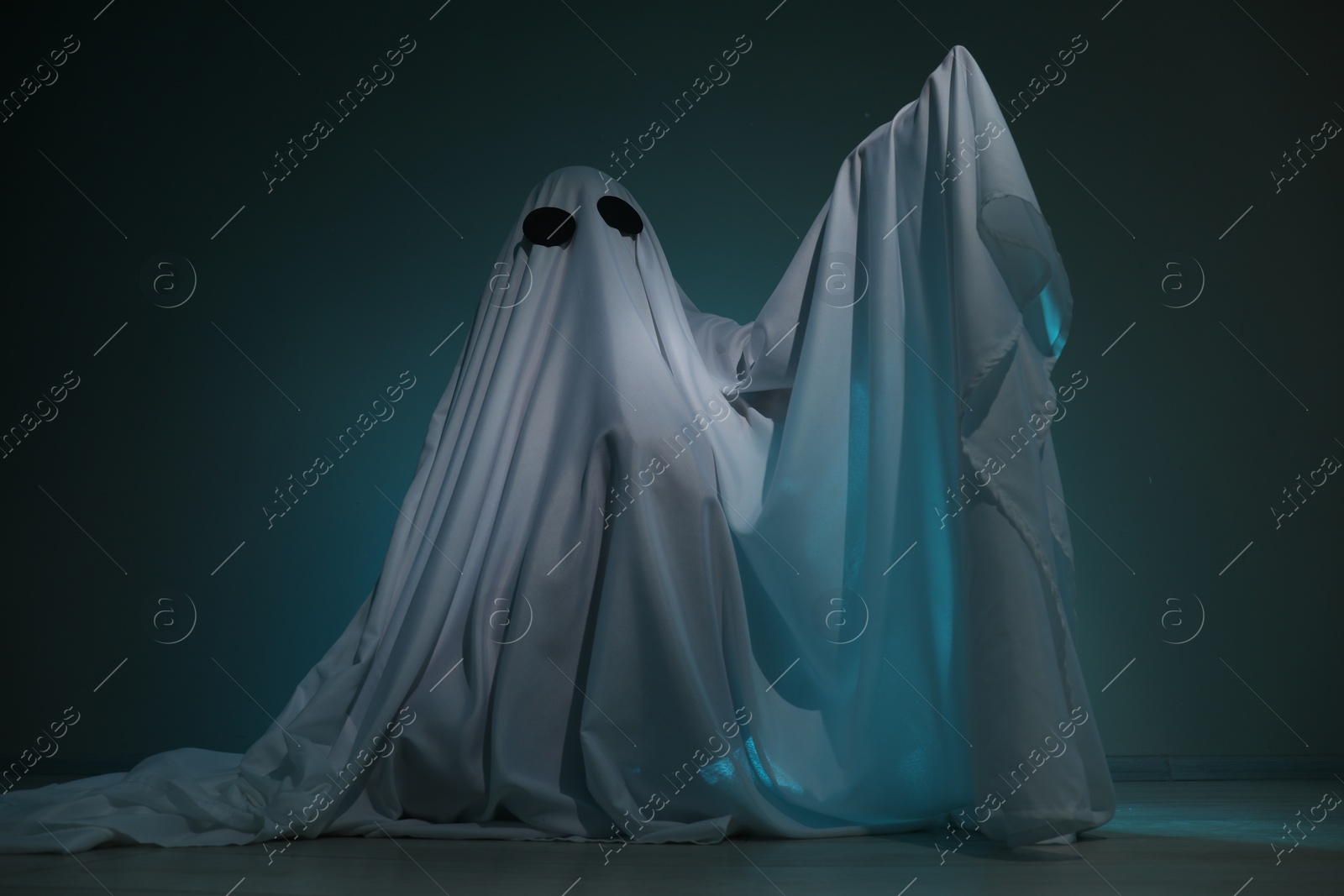 Photo of Creepy ghost. Woman covered with sheet on dark teal background