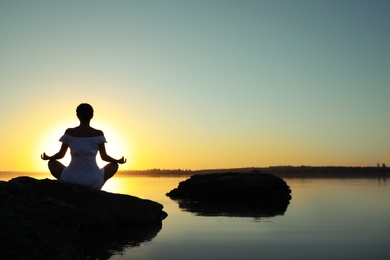 Woman practicing yoga near river on sunset. Healing concept