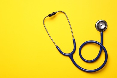 Stethoscope on yellow background, top view. Space for text