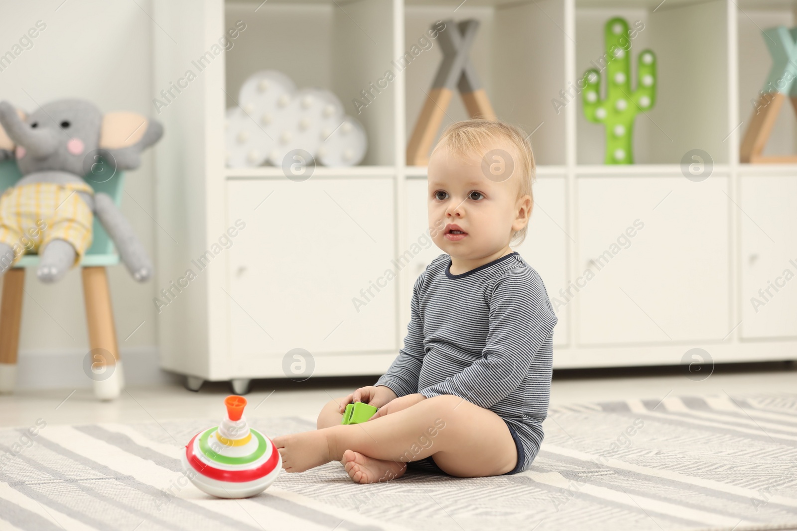 Photo of Children toys. Cute little boy with toy car and spinning top on rug at home