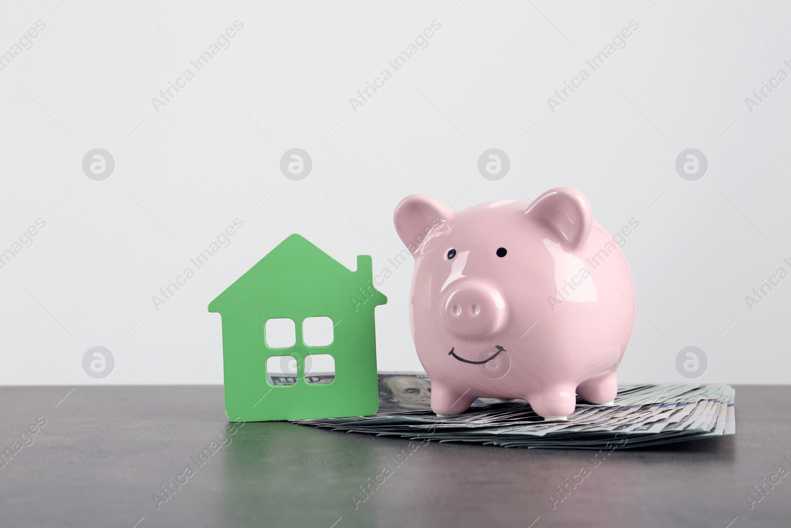 Photo of Piggy bank with dollars near toy house against white background