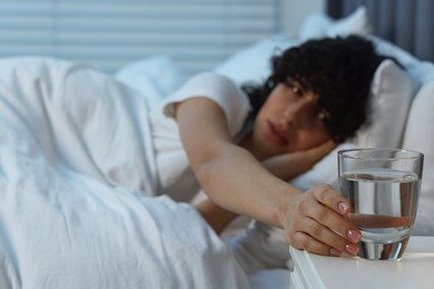 Photo of Young woman with glass of water suffering from headache in bed at night, selective focus