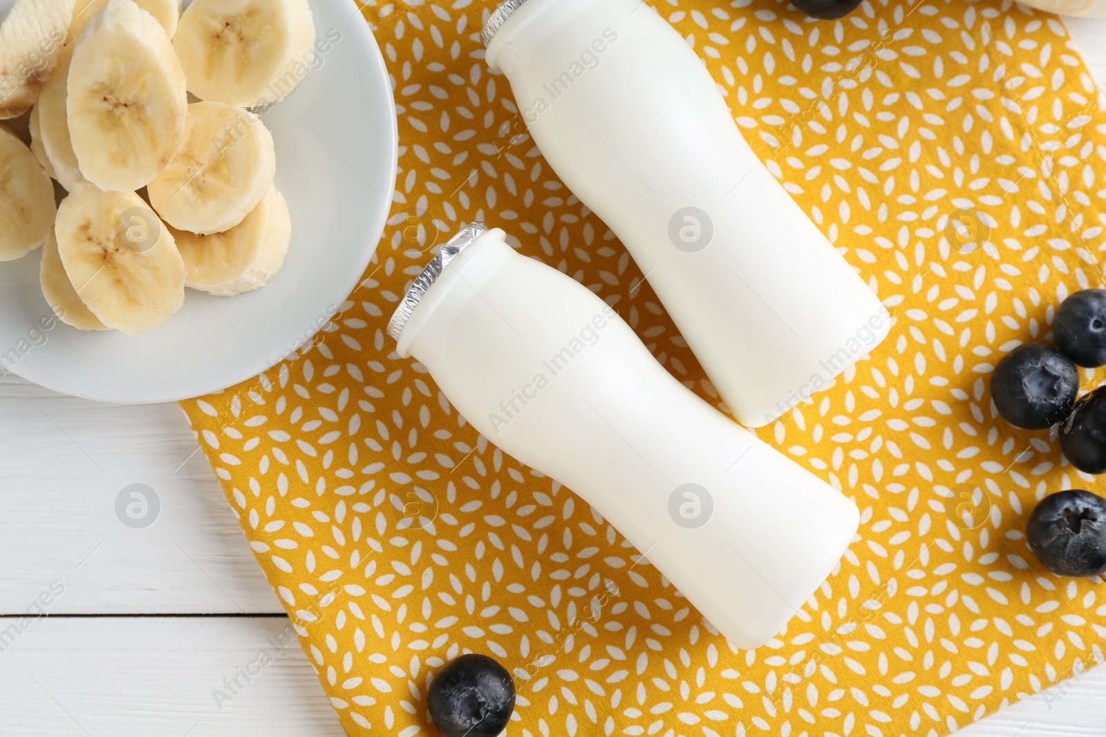 Photo of Tasty yogurt in bottles, banana and blueberries on white wooden table, top view